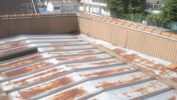 三方を壁に囲まれた、勾配のない平らなアルミ瓦棒屋根の全景